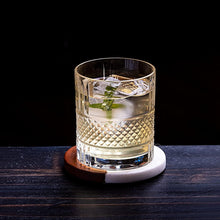 Stylish whiskey glass with ice and mint on a wooden and ceramic coaster for a sophisticated barware experience.