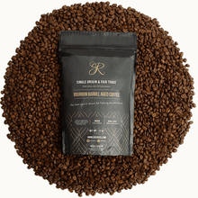 Bourbon Barrel Aged Coffee bag surrounded by roasted coffee beans, showcasing premium fair trade blend.