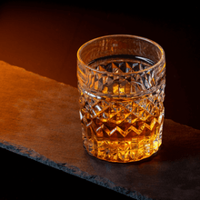 Crystal whiskey glass filled with golden whiskey on a dark slate background, perfect for cocktails and spirits.