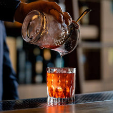 Bartender pouring a cocktail into an elegant whiskey glass showcasing craftsmanship and style.