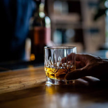 Elegant whiskey glass on wooden table, showcasing rich bourbon with chilling stones, perfect for gifting and barware.