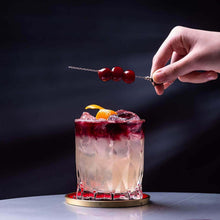 Hand garnishing a cocktail in a whiskey glass, showcasing vibrant colors and creative presentation.